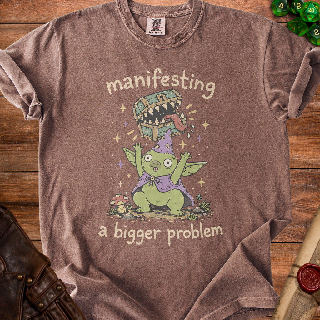 T-shirt with goblin character, wizard hat, and text "manifesting a bigger problem".