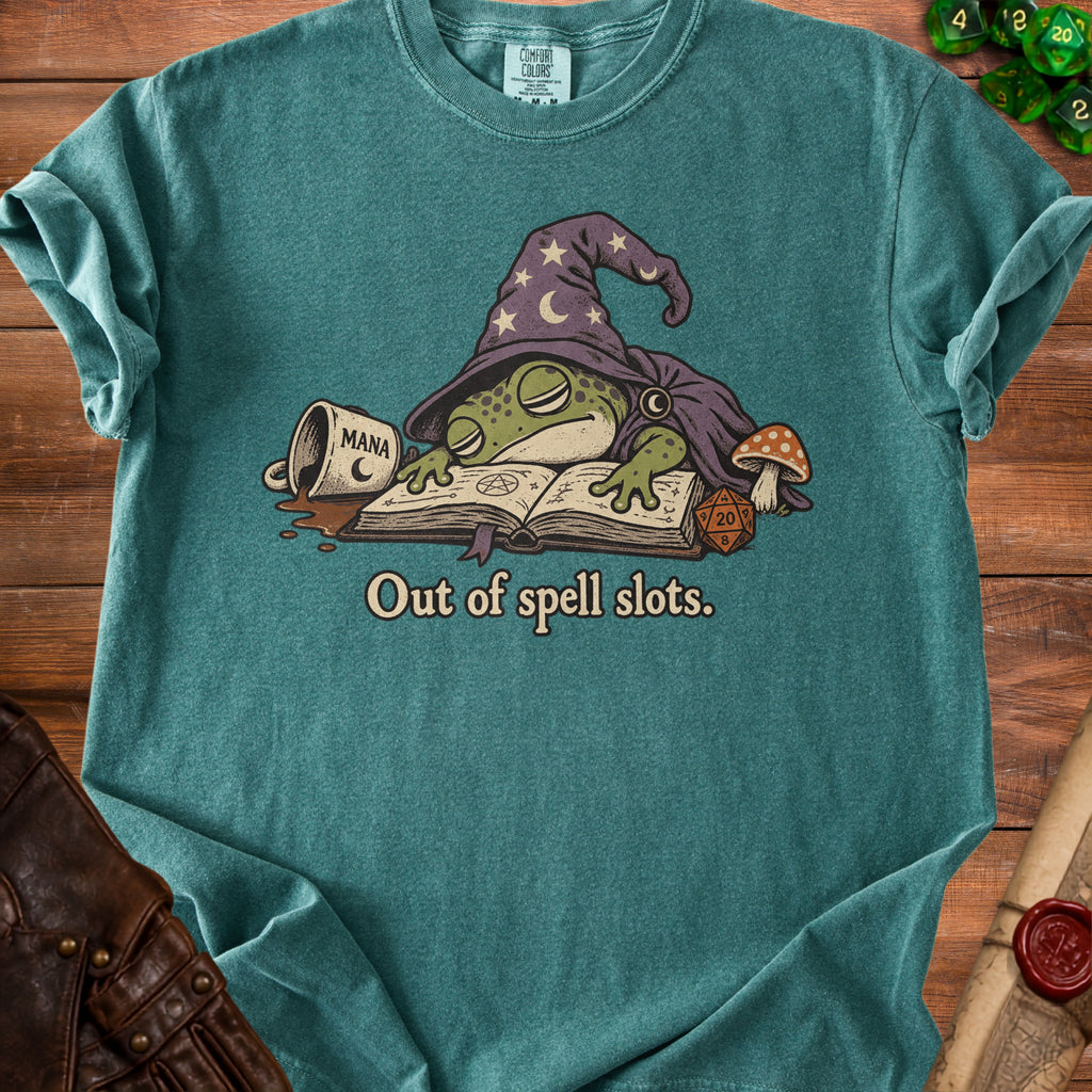 Green t-shirt with a frog wizard sleeping on a book, next to a spilled coffee mug and dice.