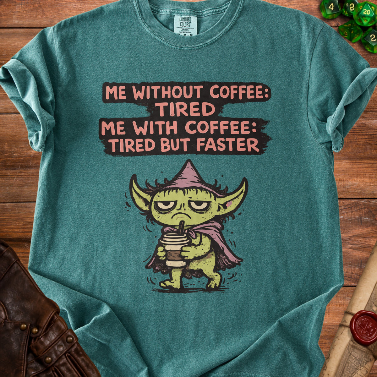 Teal t-shirt with green creature holding coffee and text "Me without coffee: tired. Me with coffee: tired but faster."