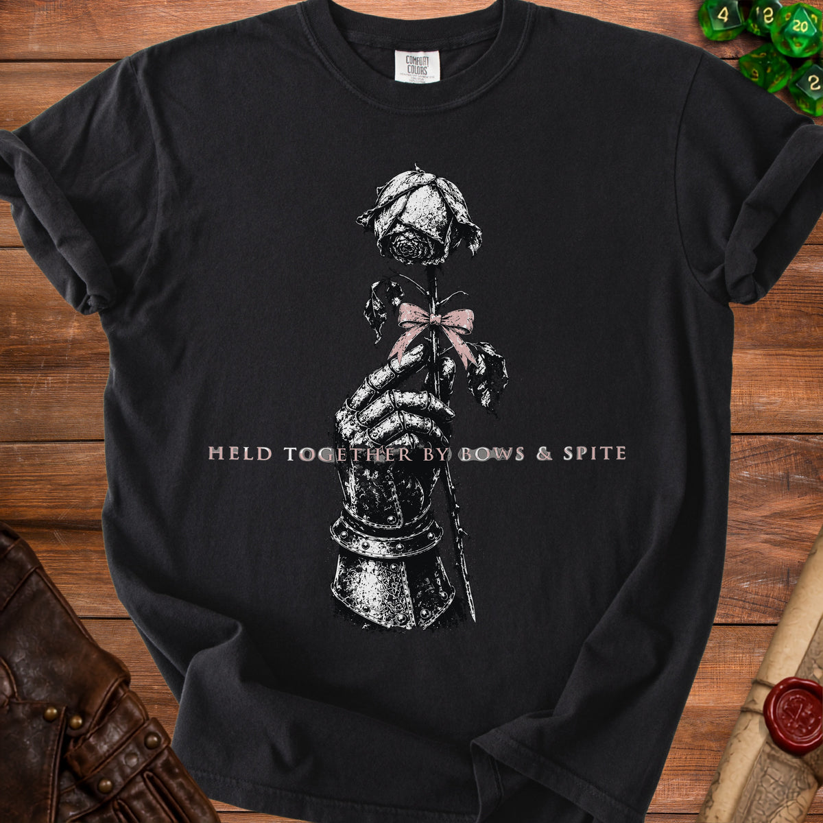 Black t-shirt with a skeletal hand holding a rose with pink bow. Text reads: "HELD TOGETHER BY BOWS & SPITE".