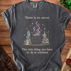 Dark grey t-shirt with a witch's cauldron, crystals, and the text "There is no secret. The only thing you have to do is continue."