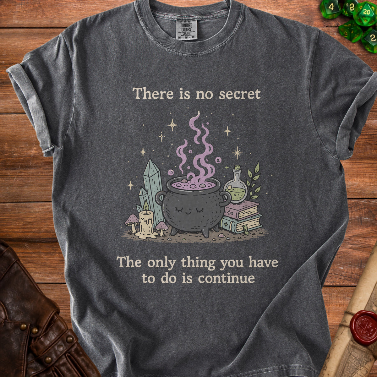 Dark grey t-shirt with a witch's cauldron, crystals, and the text "There is no secret. The only thing you have to do is continue."