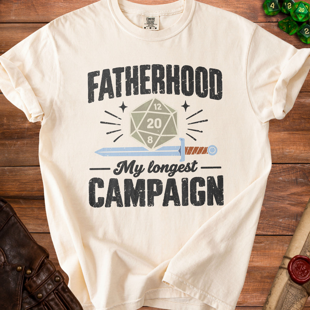 Cream t-shirt with "FATHERHOOD My longest CAMPAIGN" and D20 dice graphic.