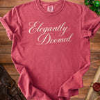 T-shirt with "Elegantly Doomed" text in cursive.