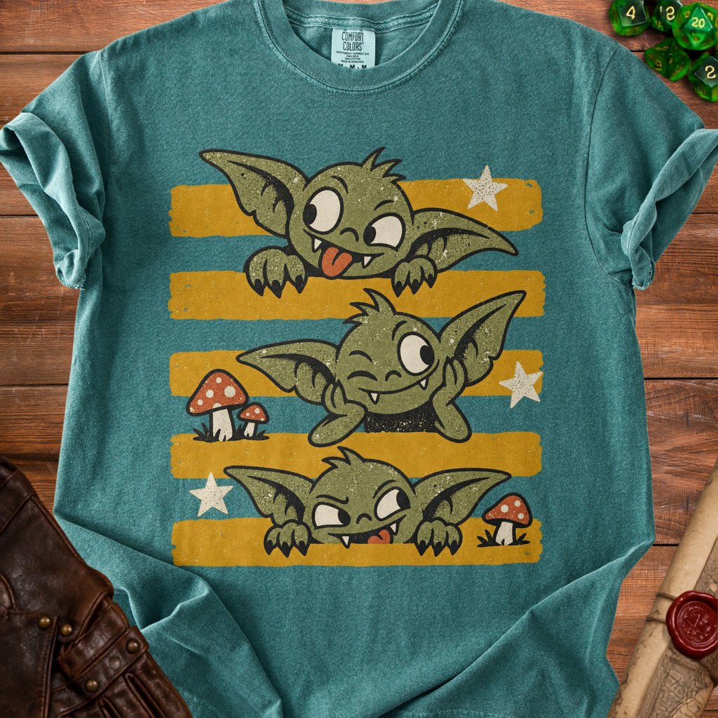 Three green goblins with stars and mushrooms on a teal t-shirt.