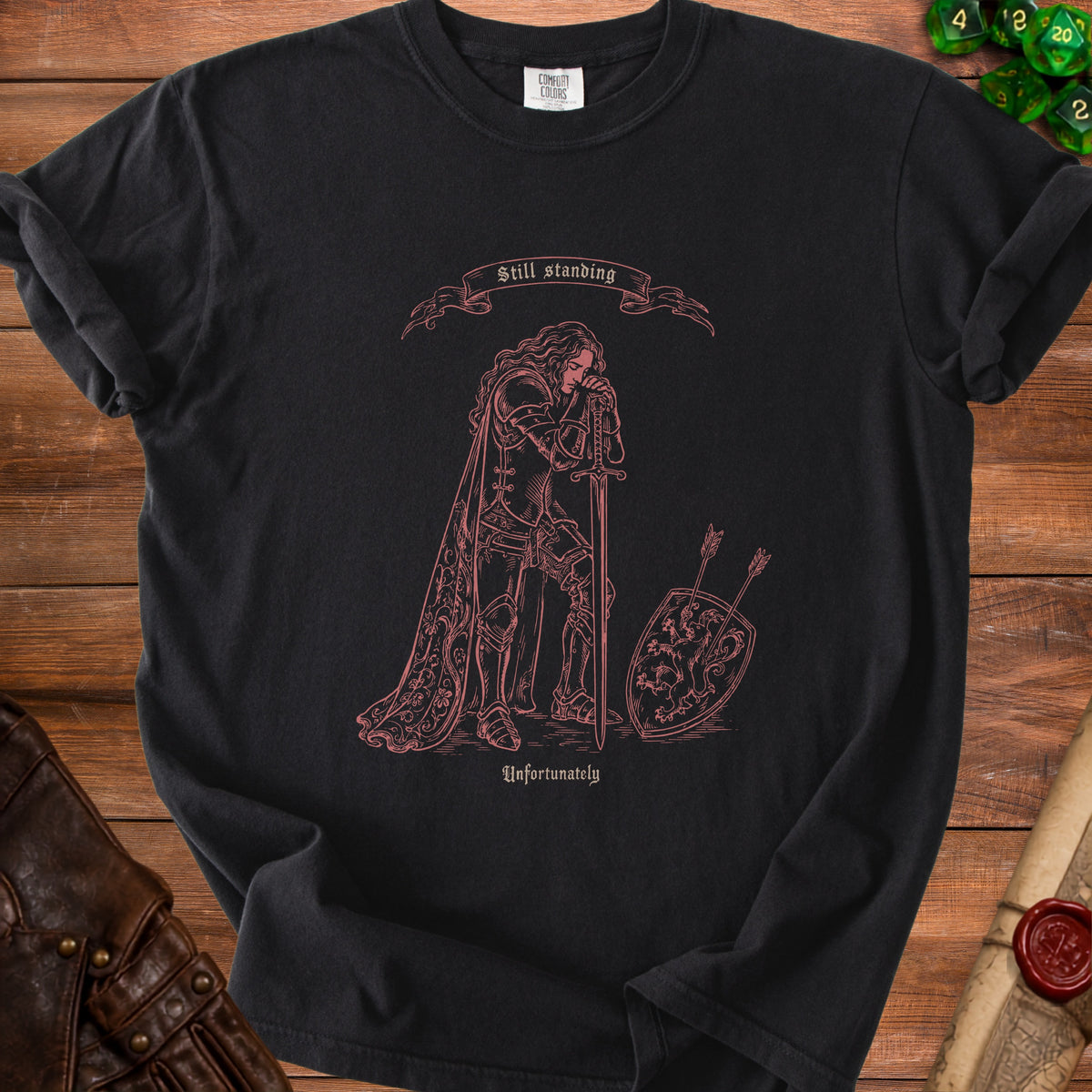 Black t-shirt with a pink line drawing of a knight and the text "Still standing" and "Unfortunately."