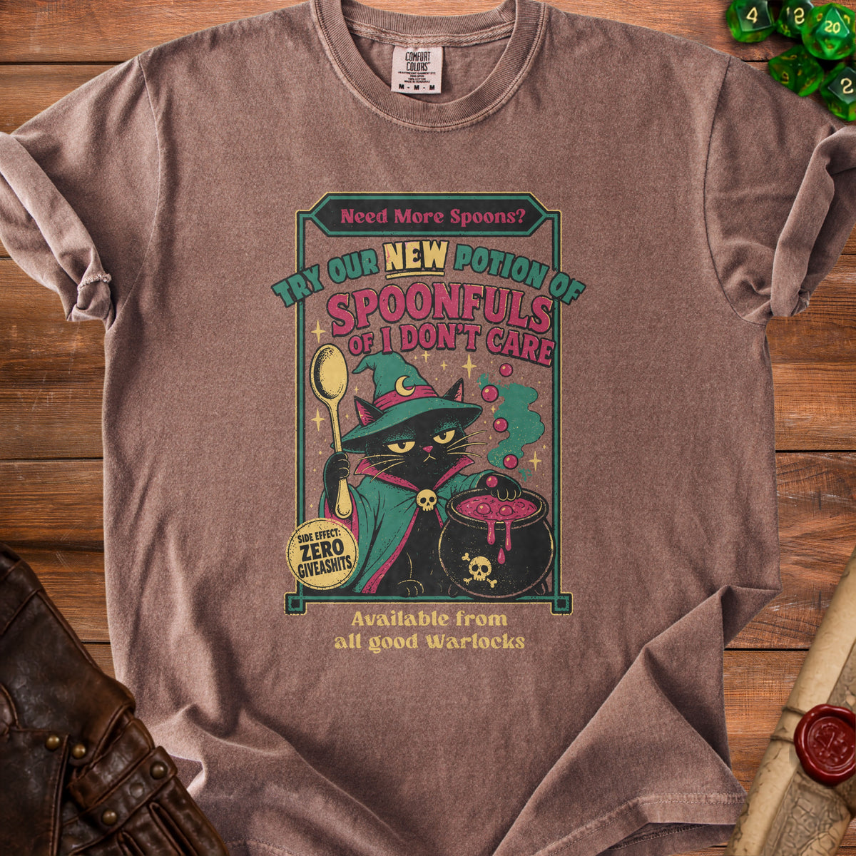 Brown t-shirt with a black cat wearing a witch hat and robe, holding a spoon near a cauldron. Text reads "Need More Spoons? Try our new potion of Spoonfuls of I don't care."