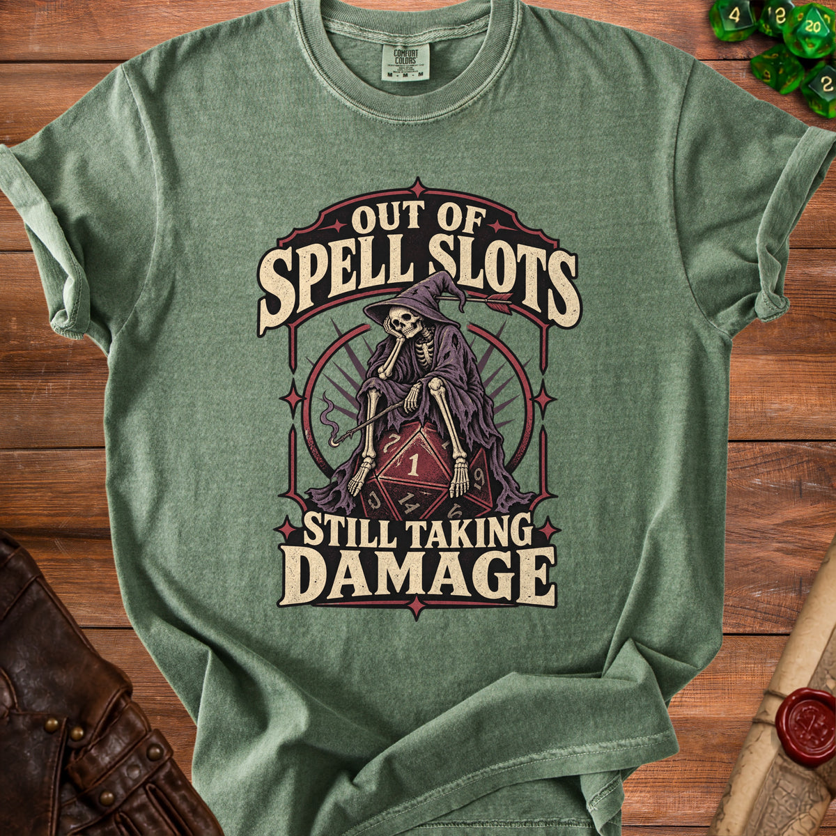 Green t-shirt with skeleton in wizard hat on D20 dice, text reads "Out of Spell Slots Still Taking Damage".
