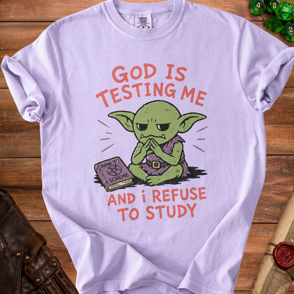 Purple t-shirt with a green goblin and text reading "GOD IS TESTING ME AND I REFUSE TO STUDY".