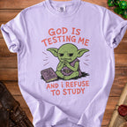 Purple t-shirt with a green goblin and text reading "GOD IS TESTING ME AND I REFUSE TO STUDY".