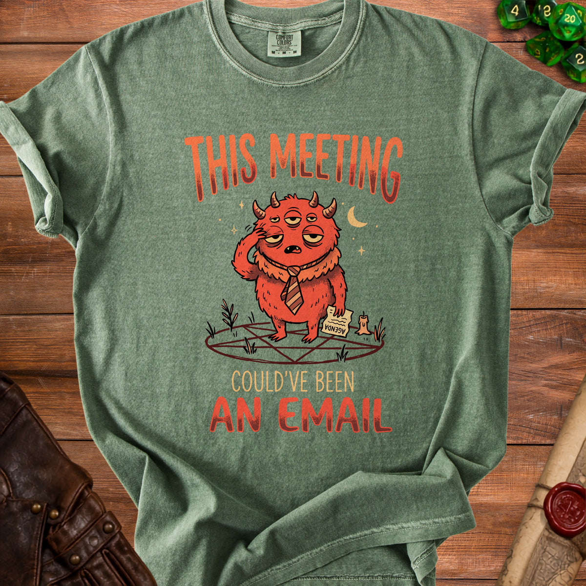 Green t-shirt with distressed print of a tired, multi-eyed monster on a pentagram with "This meeting could've been an email."
