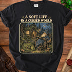 Black t-shirt with "A Soft Life In A Cursed World" text over wizard, dragon, and cottage scene.