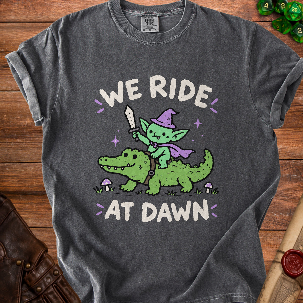 Dark gray t-shirt with graphic of goblin riding alligator and text "WE RIDE AT DAWN."