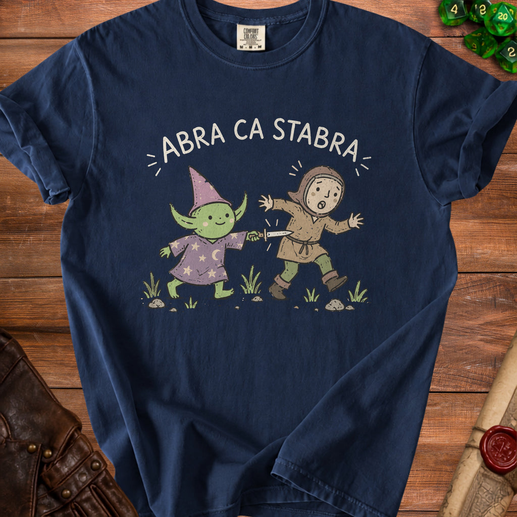 Navy t-shirt with a cartoon of a goblin wizard stabbing a surprised knight with the text "ABRA CA STABRA".