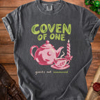 Dark t-shirt with "COVEN OF ONE" text, pink teapot, teacup, and candle graphic.