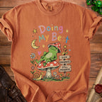 Orange t-shirt with frog on mushroom, moon, and text "Doing My Best".