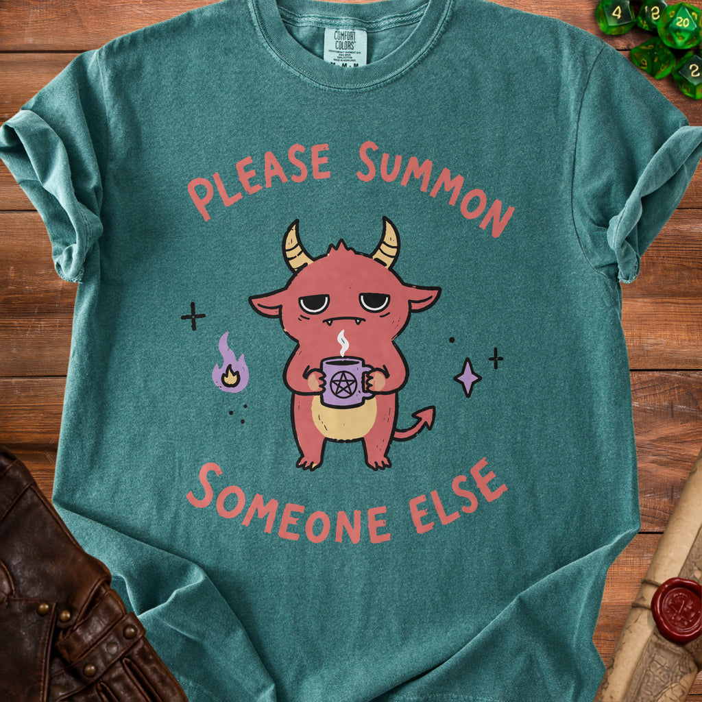 Teal t-shirt with a cartoon demon holding a pentagram mug and text "PLEASE SUMMON SOMEONE ELSE".