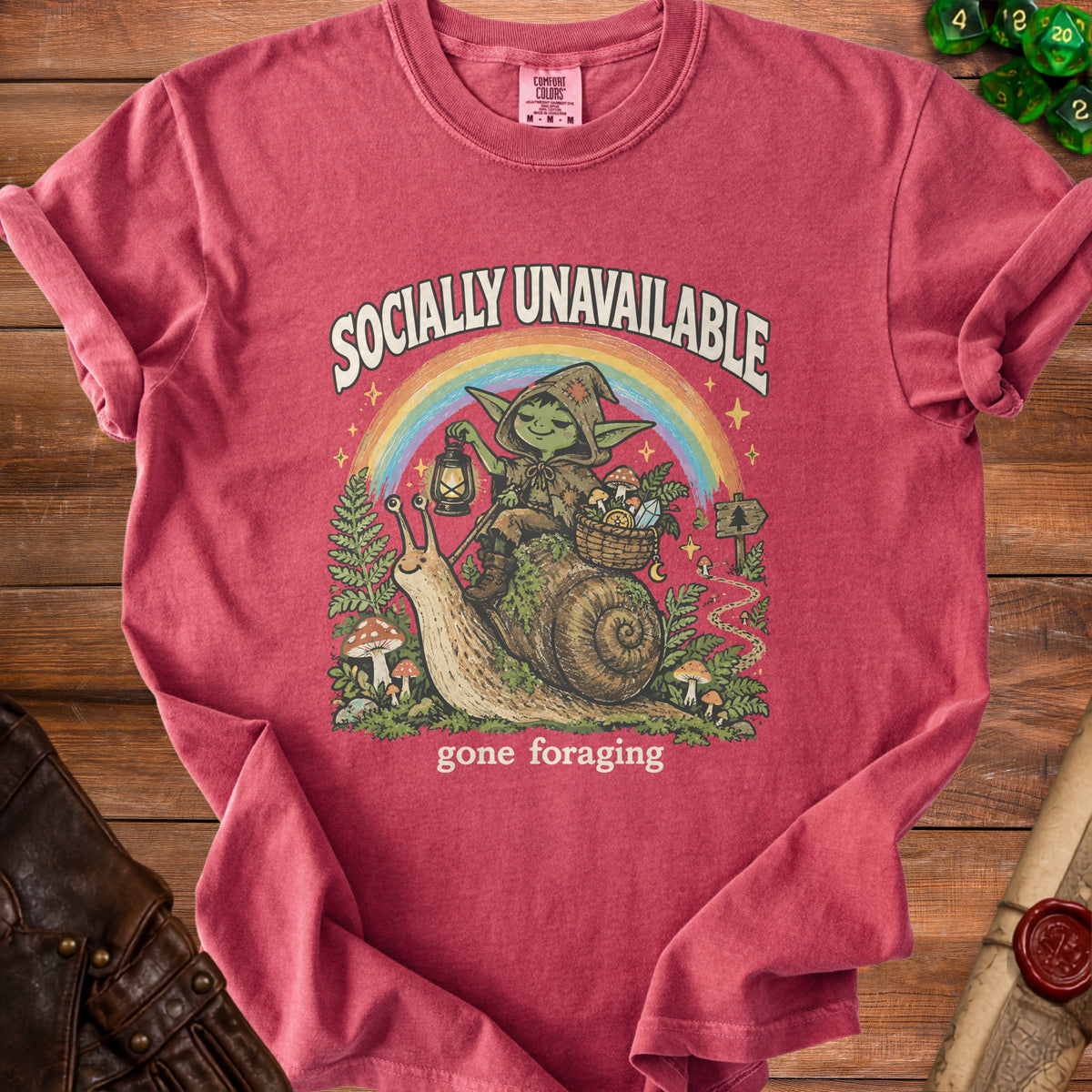 T-shirt graphic of a goblin riding a snail under a rainbow with "Socially Unavailable" and "gone foraging" text.