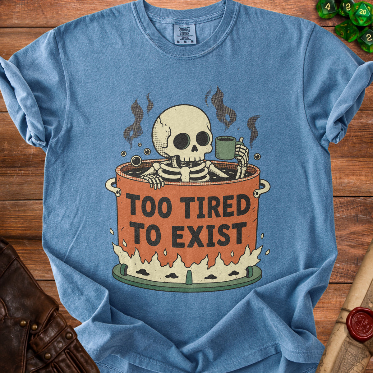 Skeleton in pot with coffee and text "Too Tired To Exist" on blue shirt.