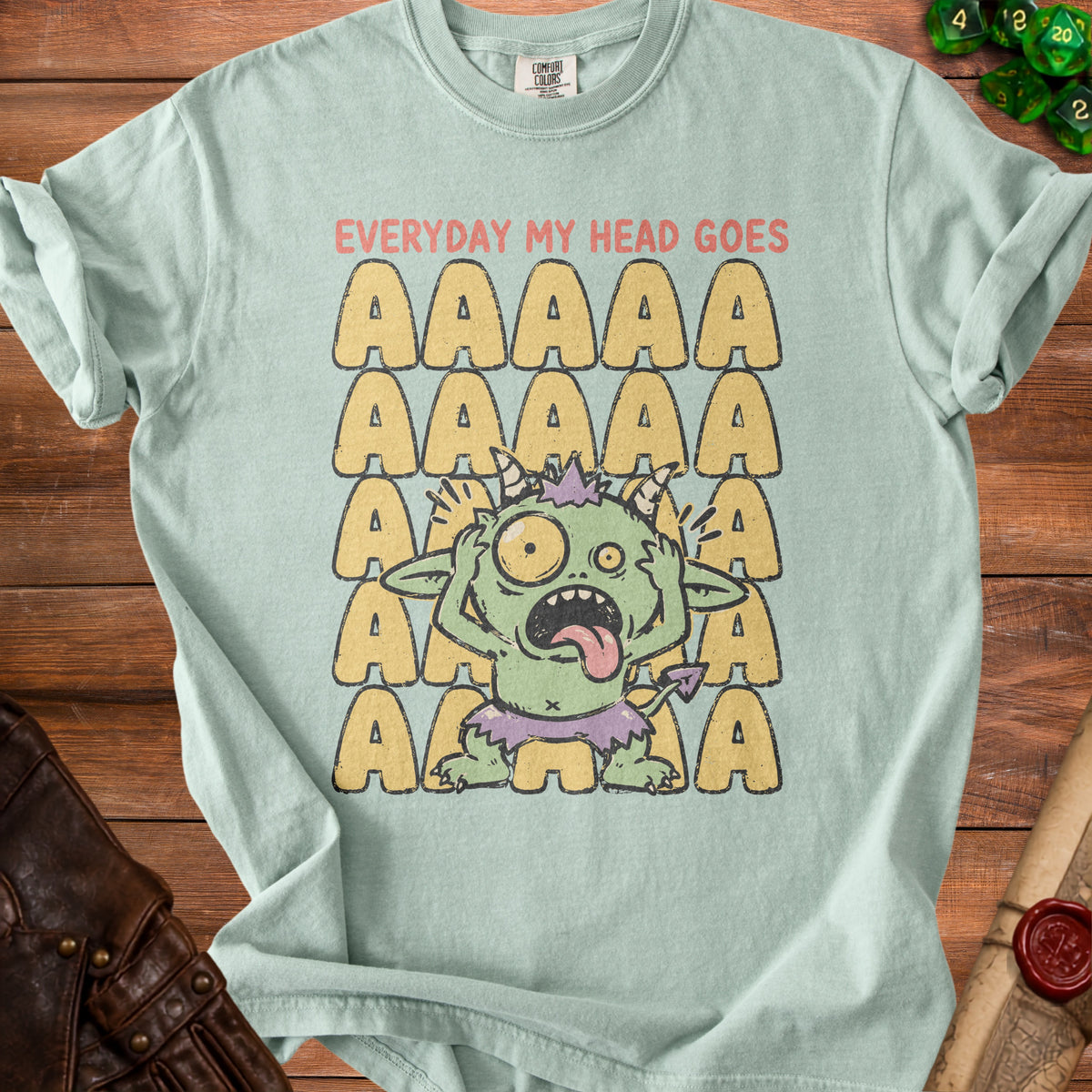 Green monster graphic on a light blue t-shirt with "EVERYDAY MY HEAD GOES" and rows of "A"s.