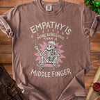 Brown t-shirt with skeleton on skateboard and text "EMPATHY IS MORE REBELLIOUS THAN A MIDDLE FINGER".