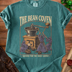 The Bean Coven t-shirt features figures operating a coffee grinder and the text "Gather for the Daily Grind".