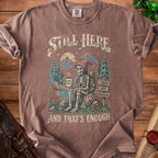 Skeleton enjoying coffee in a forest landscape with text "STILL HERE" and "AND THAT'S ENOUGH".