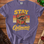 Purple t-shirt with text "STAY Optimimic" featuring a monster treasure chest graphic.