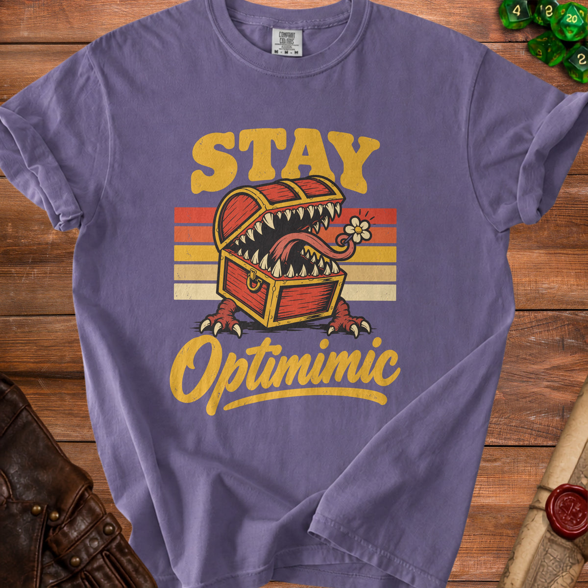 Purple t-shirt with text "STAY Optimimic" featuring a monster treasure chest graphic.