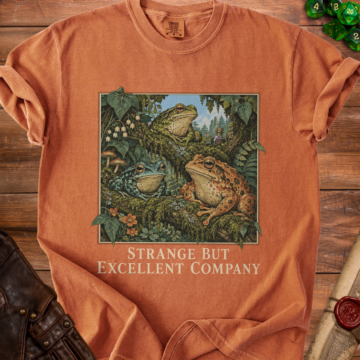 Orange t-shirt with three frogs in forest and text "Strange But Excellent Company".