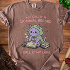 Brown t-shirt with purple cat character writing "You call it a criminal record, I call it my lore."
