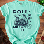 Mint green t-shirt with a possum holding a D20 dice and the text "Roll like you mean it."
