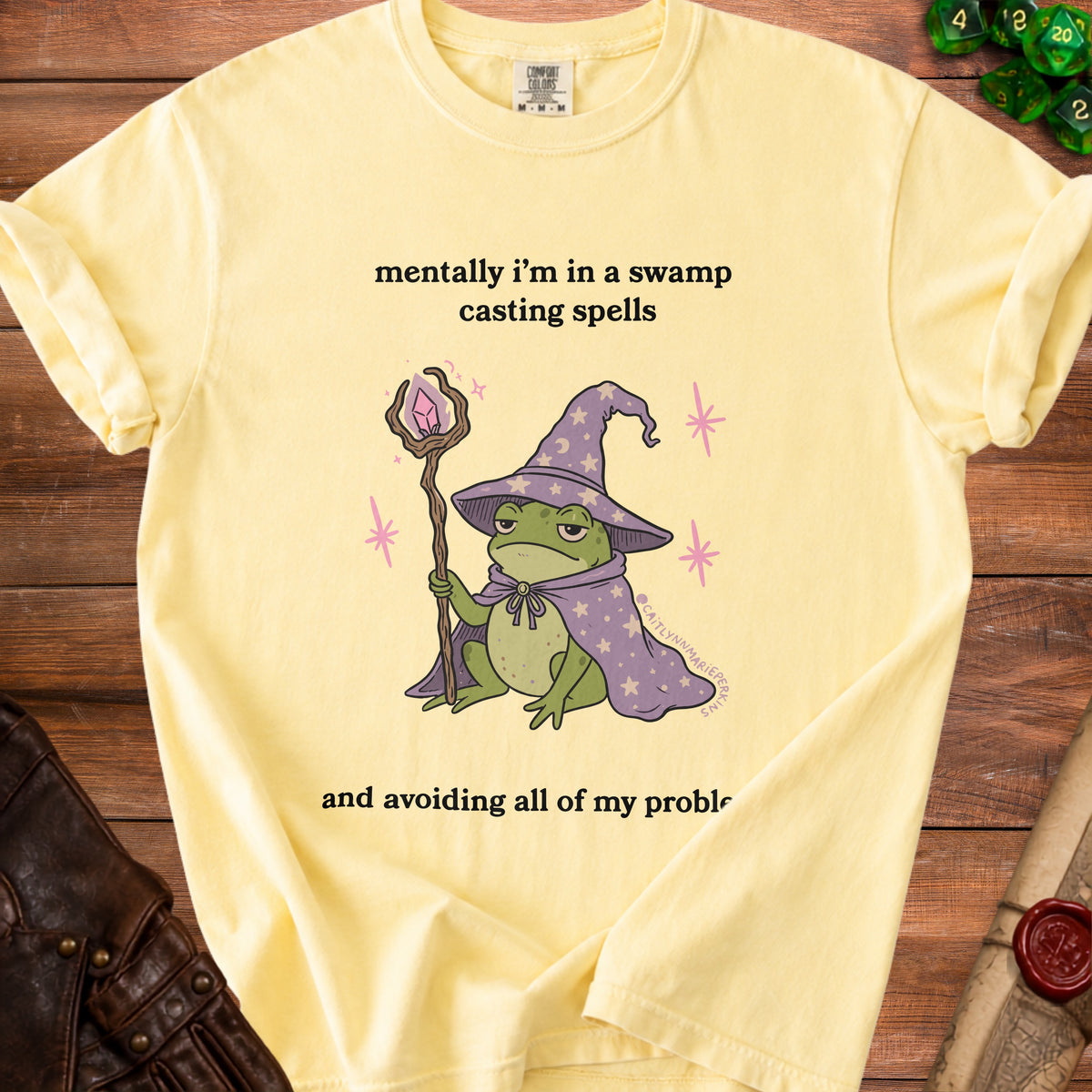 Light yellow t-shirt with a cartoon frog wizard casting spells and avoiding problems.