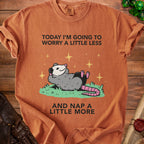 T-shirt with graphic of opossum lounging and text "Today I'm going to worry a little less and nap a little more."