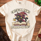Cream t-shirt with a black cat wearing a wizard hat and "Critical Paws Running on Vibes" text.
