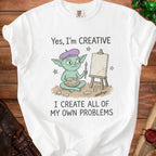 White t-shirt with a cartoon goblin artist and the text "Yes, I'm CREATIVE I CREATE ALL OF MY OWN PROBLEMS".