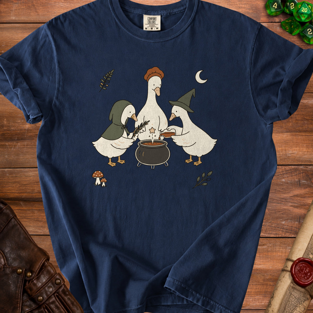 Three cartoon geese perform a potion ceremony around a cauldron on a navy blue t-shirt.