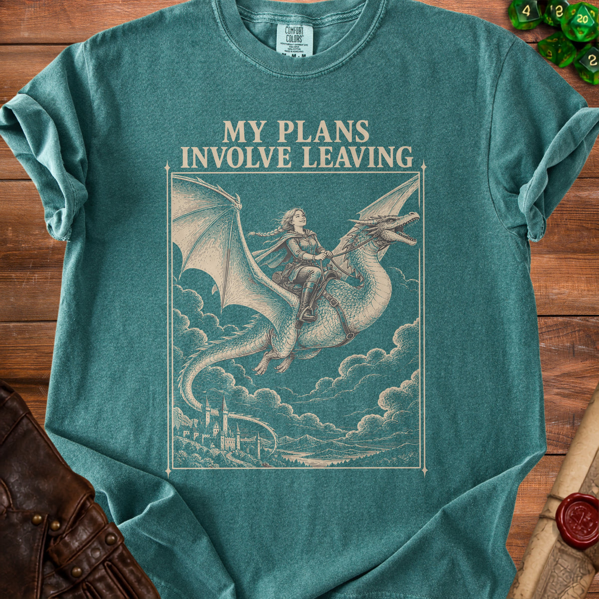 Teal t-shirt featuring a beige graphic of a woman riding a flying dragon above a castle, with the text MY PLANS INVOLVE LEAVING.