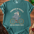 Green t-shirt with wizard riding a bike graphic and text "POWERED BY PEDALS AND QUESTIONABLE MAGIC".