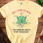 Yellow t-shirt with a green character looking at a scroll that says "HORRORS".