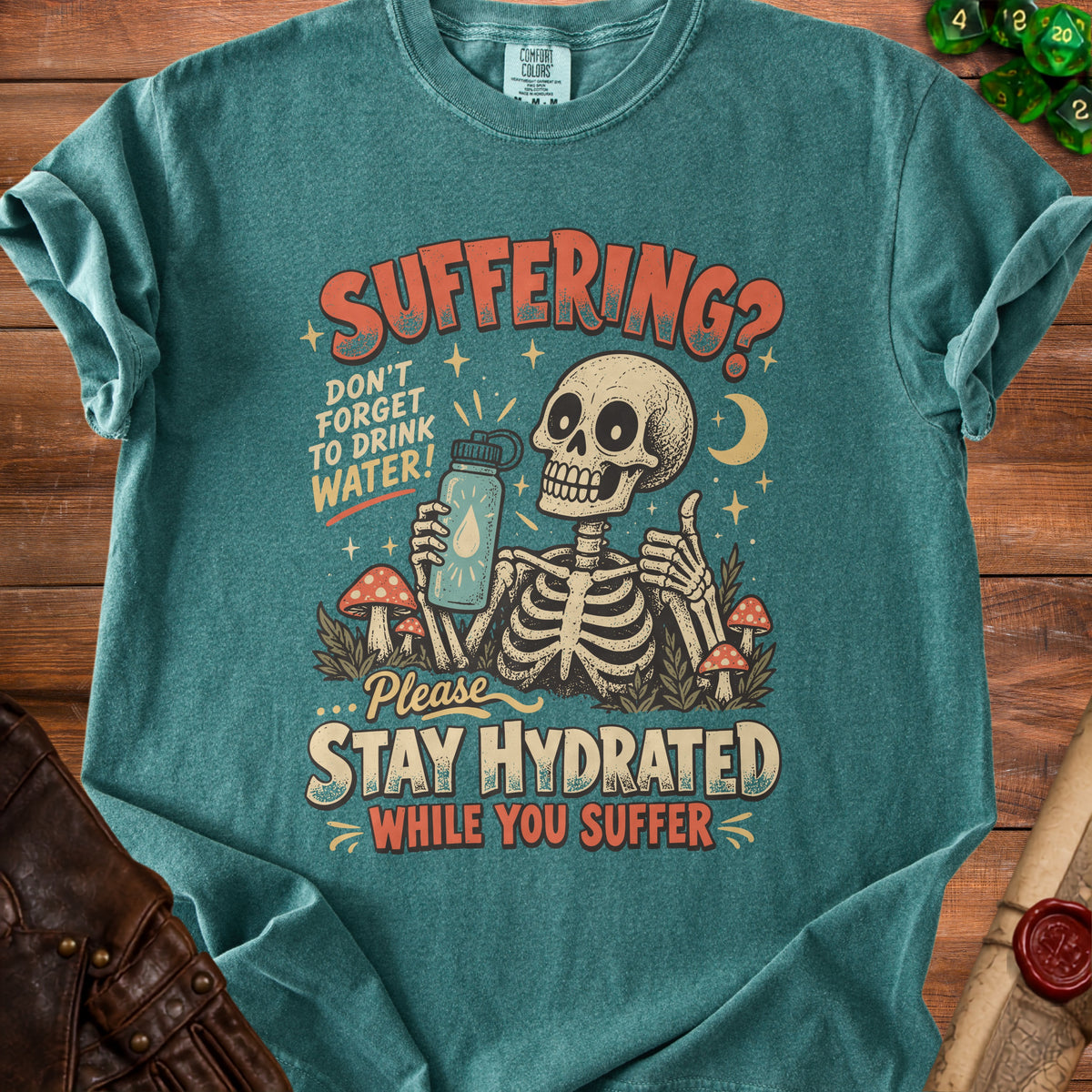 A teal t-shirt featuring a skeleton drinking water, mushrooms, and the text staying hydrated while suffering.