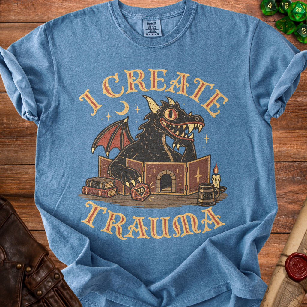 Blue t-shirt with a black dragon behind a game master screen, text "I CREATE TRAUMA".