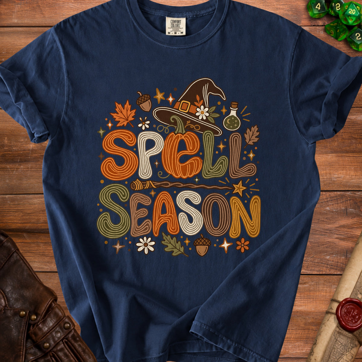 Dark blue t-shirt with "Spell Season" in retro font, witch hat, pumpkin, and fall leaves.