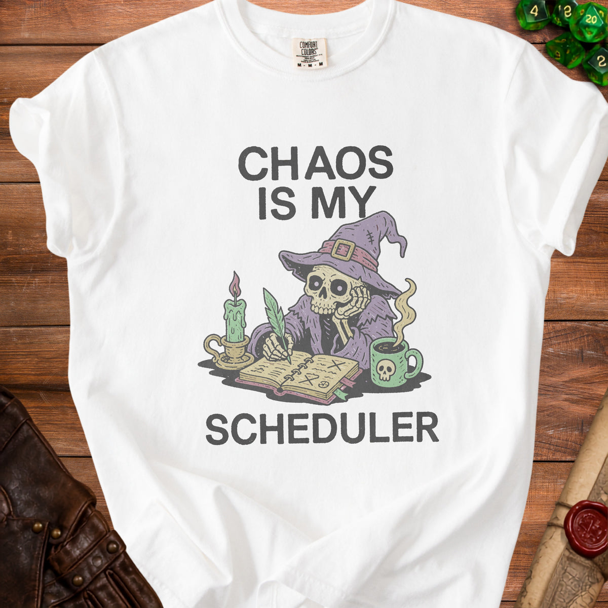 White t-shirt with skeleton writing "Chaos Is My Scheduler" with a skull mug.