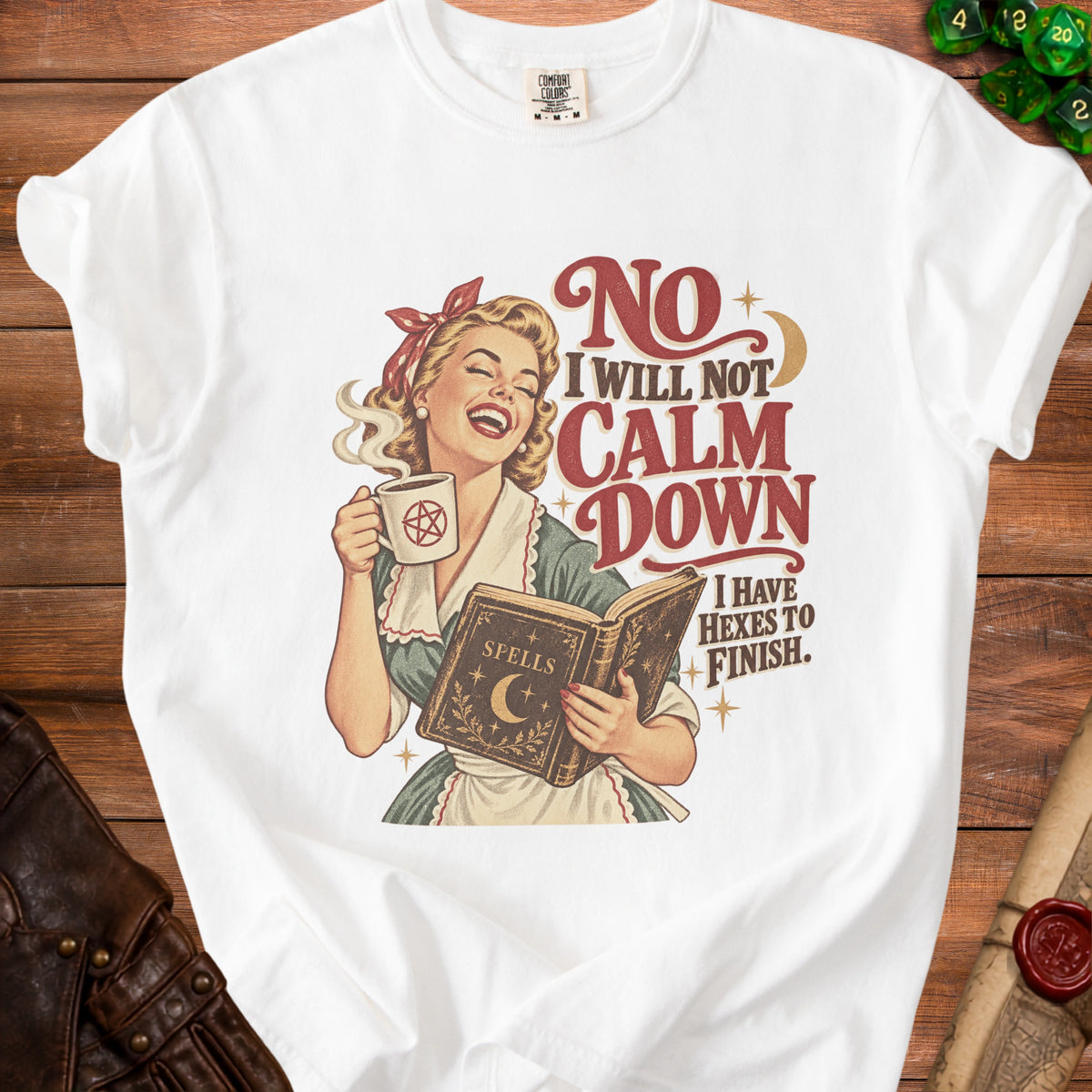 A white t-shirt featuring a retro illustration of a woman reading a spellbook while holding a mug.