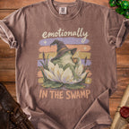 Brown t-shirt with graphic of frog in witch hat holding coffee, text "emotionally IN THE SWAMP".