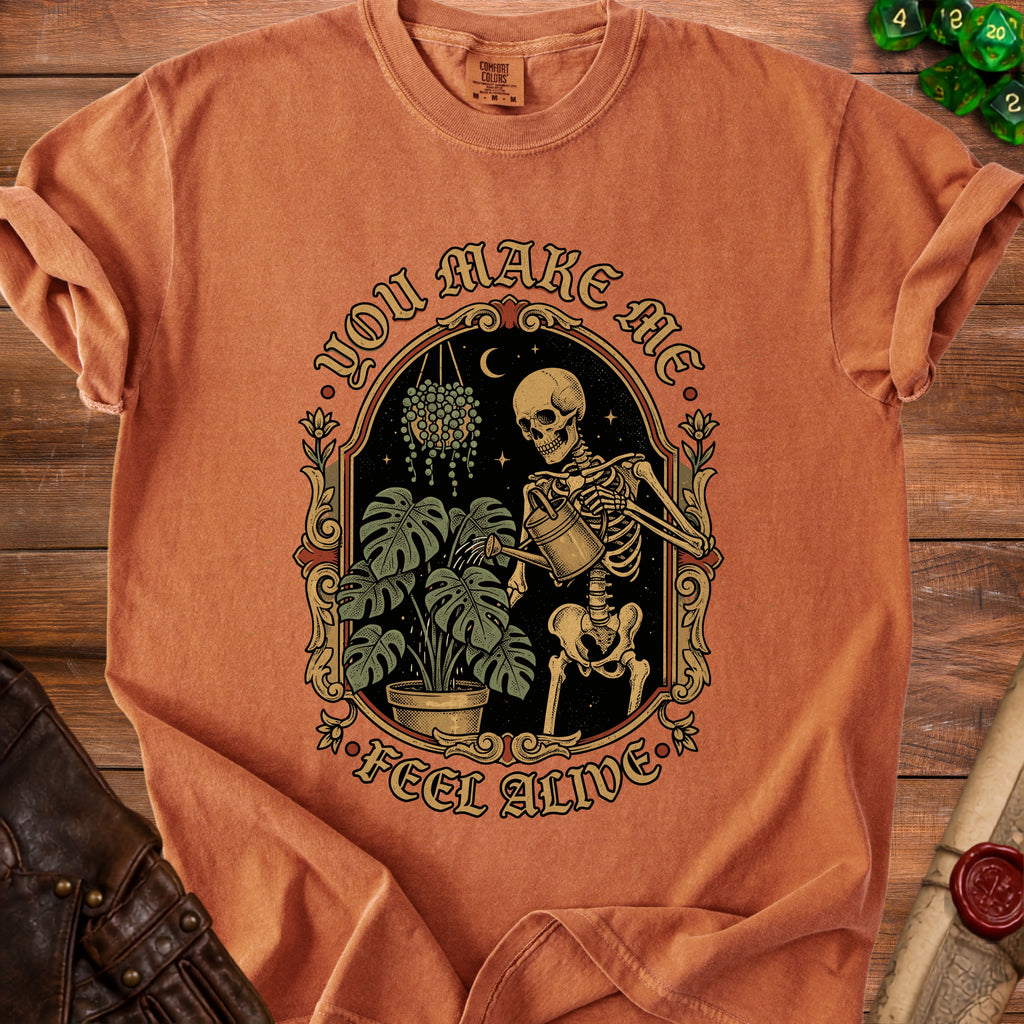 Orange t-shirt with skeleton watering plants and "You Make Me Feel Alive" text.