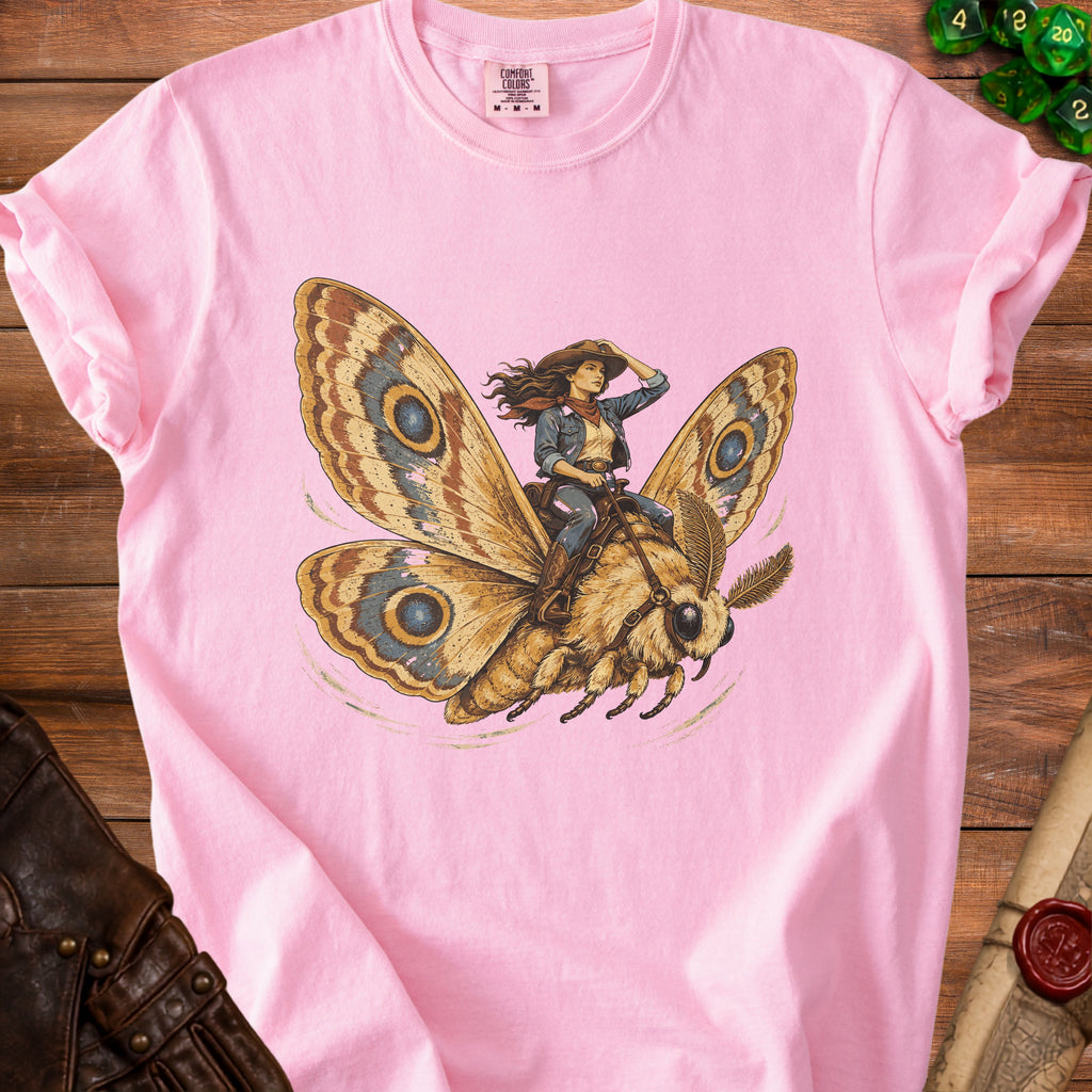 Illustration of a cowgirl riding a large moth on a pink t-shirt.