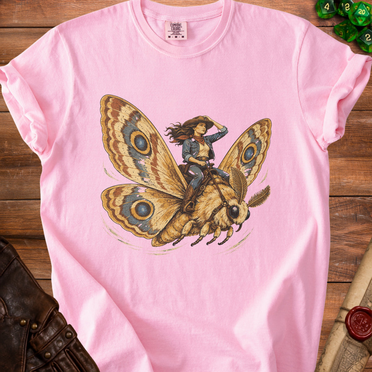 Illustration of a cowgirl riding a large moth on a pink t-shirt.