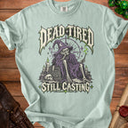Light blue t-shirt featuring a skeleton wizard with text "DEAD TIRED STILL CASTING."